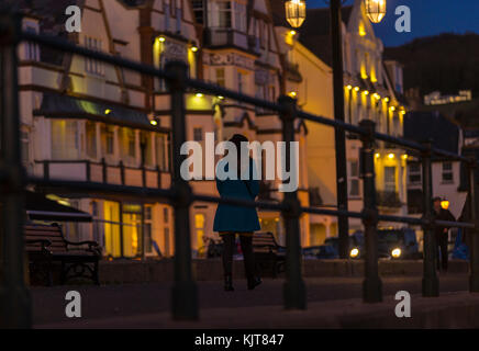 Allein eine Frau spaziert an der Esplanade bei Sidmouth entlang, während der Abend fällt. Stockfoto