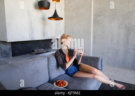 Blonde Frau hält Handy und isst reife Erdbeere, sitzen Stockfoto