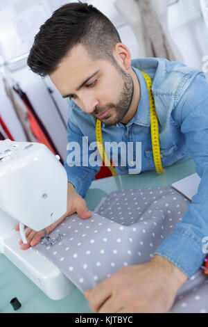 Oung Mann das Nähen eines Kleides in seinem Studio Stockfoto