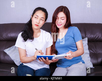 Zwei junge Frau ein Buch auf dem Sofa im Wohnzimmer zu Hause schreiben Stockfoto