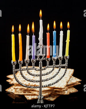 Menorah mit brennenden Kerzen für chanukka auf einem schwarzen Hintergrund. matza im Hintergrund. Stockfoto