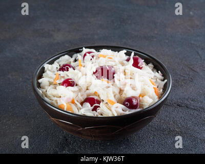 Traditionelle russische Vorspeise Sauerkraut mit Cranberry und Karotte in dunklen Schüssel auf schwarzem Zement Hintergrund. Fermentierter Kohl. Russische Küche und Rus Stockfoto