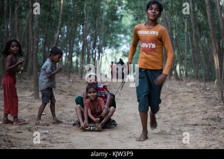 23. November 2017 - Cox's Bazar, Bangladesch - Rohingya-Jungs spielen auf einem selbstgemachten Go-Kart durch den bewaldeten Weg im Flüchtlingslager. Das Kutupalong Refugee Camp ist ein Flüchtlingslager in Ukhia im Cox's Bazar-Gebiet in Bangladesch, das hauptsächlich den Rohingya-Muslimen, die vor religiöser Verfolgung in Myanmar geflohen sind, zum Opfer fällt. Das UNHCR schätzte, dass sich Ende 2017 mindestens 30.000 Flüchtlinge im Lager aufhielten. Quelle: Marcus Valance/SOPA/ZUMA Wire/Alamy Live News Stockfoto