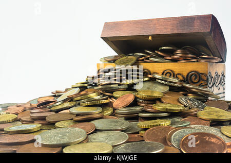 Eine kleine hölzerne Schatztruhe, die ist voller Münzen auf einem weißen Hintergrund. Isolierte Zusammensetzung, die zur wirtschaftlichen und finanziellen verbunden ist Stockfoto