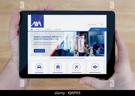 Ein Mann schaut auf die AXA Website auf seinem iPad tablet device, Schuß gegen einen hölzernen Tisch top Hintergrund (nur redaktionelle Nutzung) Stockfoto