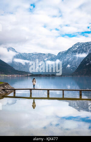 Zen Momente Thema Bild mit einer Frau allein stehend auf einer Brücke über den Hallstätter See, durch das Schweigen und die Berge umgeben, in Österreich Stockfoto