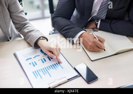 Nahaufnahme der unkenntlich Kollegen Studium finanzielle Kennzahlen, während am Schreibtisch der modernen Großraumbüro sitzen Stockfoto