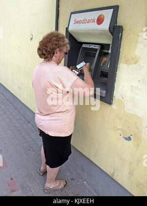 NICA, LETTLAND - 25. JUNI 2013: Ältere Frau benutzt Geldautomaten in der Ladenwand. Stockfoto