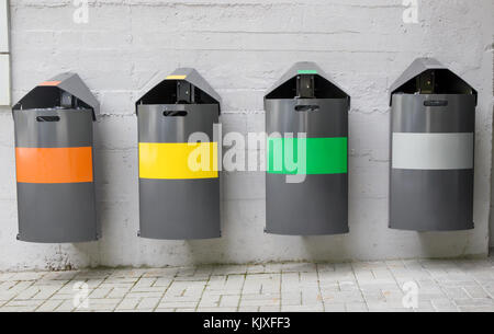 Verschiedene farbige Behälter zur Sammlung von recycelten Materialien haften an der Wand im Hintergrund. Stockfoto