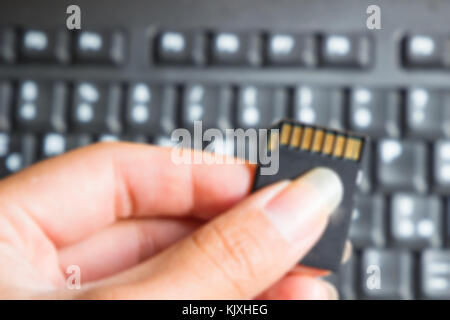 Unscharfes Bild. Hand mit einer Speicherkarte über Laptop Tastatur Hintergrund, Kamera, Speicherkarte. Stockfoto