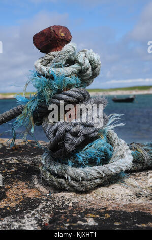 Verknotete Seil auf einem eisernen Weltbewusstseins auf einem Hafen mit traditionellen irischen Curragh im Hintergrund Stockfoto