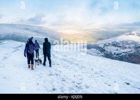 Winter wandern. Wanderer mit Hunden im Schnee auf der großen Ridge, mit Sonne in der Ferne. Peak District, Derbyshire, England, Großbritannien Stockfoto