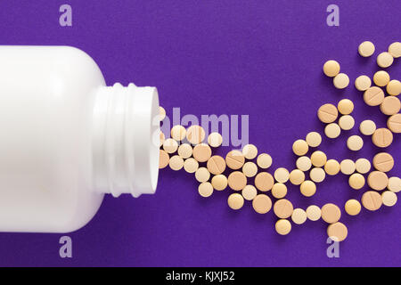 Gruppe der sortierten beige Tabletten. Kapseln verschütten aus weiße Flasche. lila Hintergrund.line, weg Kurs Konzept. Stockfoto