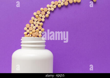 Gruppe der sortierten beige Tabletten. Kapseln verschütten aus weiße Flasche. violett unterlegt. Linie, weg Kurs Konzept. Stockfoto