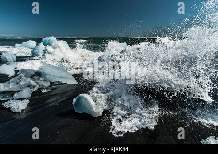 Die Wellen des Ozeans spielen mit dem Eis Blöcke auf dem schwarzen vulkanischen Strand in der Nähe der Jökulsárlón in Island abgelehnt Stockfoto