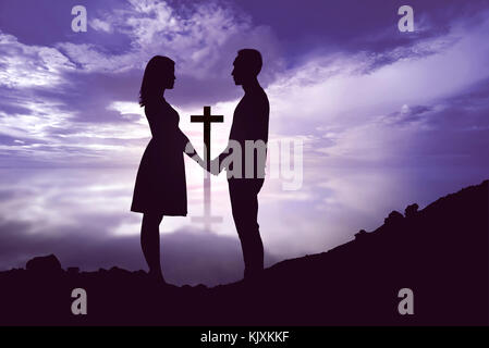 Portrait von romantisches Paar Hände halten und bei jeder anderen Suchen mit dem christlichen Kreuz gegen die drastischen Himmel Hintergrund Stockfoto