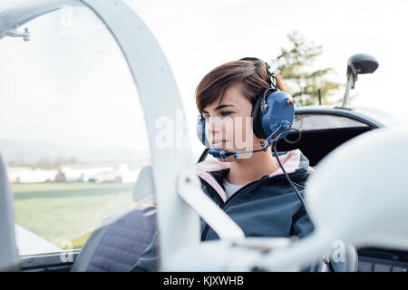 Lächelnd weibliche Piloten in der Light aircraft Cockpit, sie trägt aviator Headset und Kontrolle der Kontrollen Stockfoto