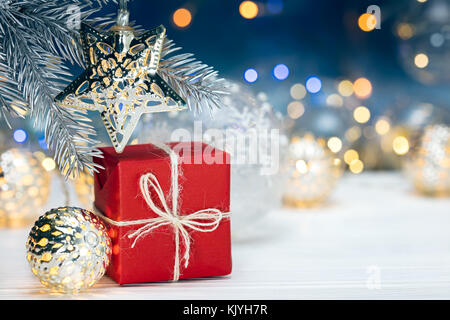 Christbaumschmuck auf Fir Tree Branch und Geschenkbox gegen verwackelte leuchten die gelben Hintergrund Stockfoto