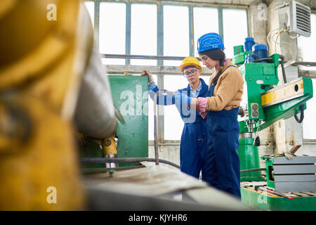Nachdenkliches Werk Mitarbeiter drücken, während Sie zusammen auf den industriellen Maschinen in der Werkstatt Stockfoto