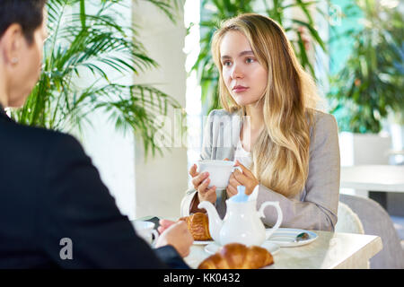 Porträt der moderne junge Frau trinkt Kaffee im Cafe Tabelle jemand sitzt ihr gegenüber während der Mittagspause Stockfoto