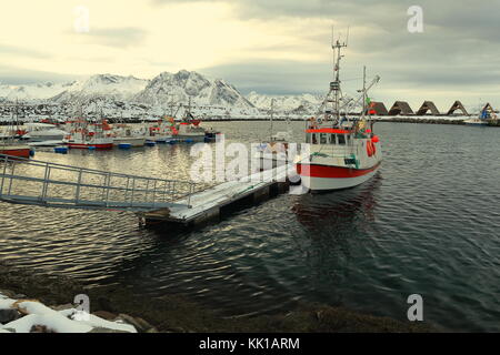 Fischerboote im Hafen festgemacht - bewölkten Himmel - Holz- Racks für die Trocknung von Fisch und schneebedeckte Berge - festvagaksla hallvarlitinden festvagtinden - Hintergrund Stockfoto