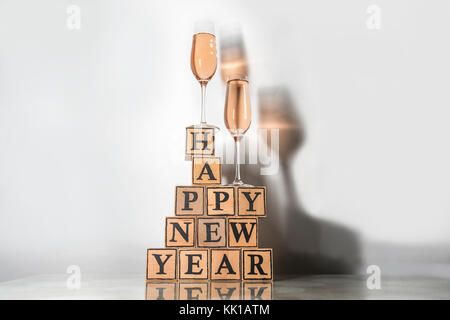 Gläser mit rosigen Champagner eine farbige Schatten und Holzwürfel machen Form der text Frohes neues Jahr Stockfoto