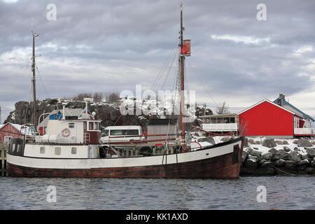 Altes Fischerboot mit Holzrumpf im Hafen vertäut. traditionellen Fischerhütten - Rorbuer jetzt rot lackiert für touristische Nutzung - stangerholmen Hügel in backgroun Stockfoto