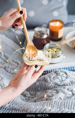 Weibliche Hände verschmiert Frischkäse mit frischem Brot. Frühstück im Bett, einem Tablett mit Käse, grissini, Marmelade und aromatische Kerze. Weihnachten Morgen. Honeymo Stockfoto