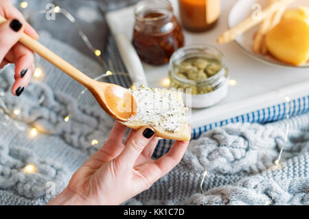 Weibliche Hände verschmiert Frischkäse mit frischem Brot. Frühstück im Bett, einem Tablett mit Käse, grissini, Marmelade und aromatische Kerze. Weihnachten Morgen. Honeymo Stockfoto