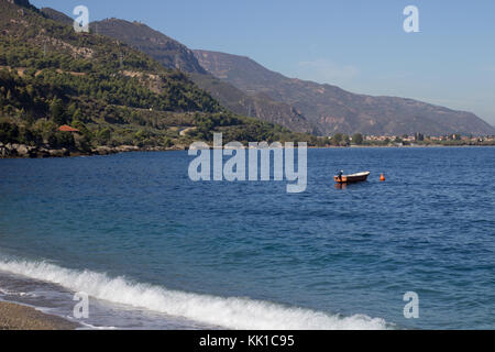 Blaues Meer und ein kleines Boot auf dem Wasser mit Wald auf den Hintergrund und die kleinen Wellen am Strand Stockfoto