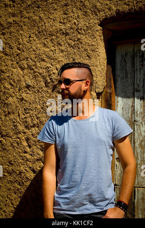 Kaukasische Mann mit Sonnenbrille auf der Seite stand vor der Tür der Schlamm Haus suchen Stockfoto