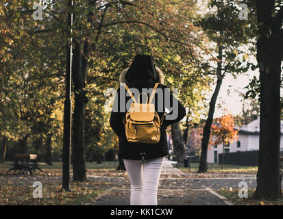 Mädchen mit Rucksack zu Fuß an einem Park mit Jacke und Gelber Sack hinter Foto von hinten Stockfoto