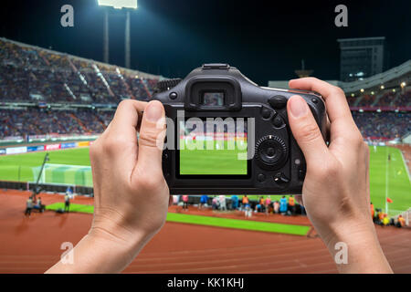 Hand mit der Kamera über Verschwommen action Fotograf, Foto bei Player in abstrakten verschwommenes Foto von Fußball-Stadion, sport Hintergrund conce Stockfoto