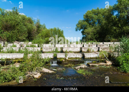 Konkrete Bausteine liegen auf einem kleinen Fluss-dam Stockfoto