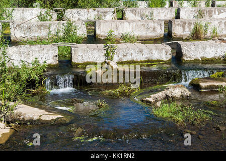 Konkrete Bausteine liegen auf einem kleinen Fluss-dam Stockfoto