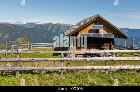 Holz- Hirte Lodge mit Solarzellen auf einem Hochland Weide mit alpinen Landschaft im westlichen Kärnten, Österreich. Stockfoto