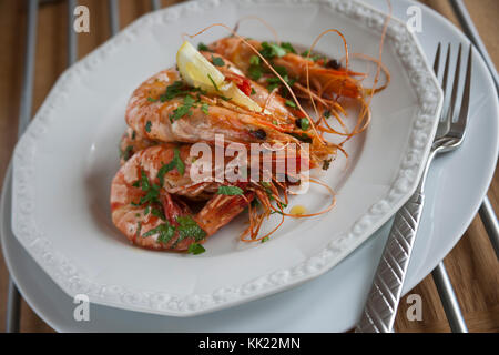 Gekochte Riesengarnelen in Tanks mit Knoblauch, Kräutern und Zitrone auf weiße Platte. Stockfoto