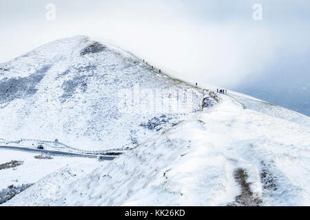 Mam Tor mit einer Decke aus Schnee und noch mehr Schnee fallen. Wanderer sind hinauf in die Wolke bedeckte Gipfel. Peak District, Derbyshire, England, Großbritannien Stockfoto