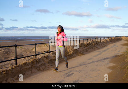 Frau, die an der Strandpromenade in Crosby, Merseyside, läuft. Wetter in Großbritannien. November 2017. Hell und sonnig an der Westküste der Mersey-Mündung. Dieses Küstengebiet um den Crosby Beach und den Crosby Marine Park erstreckt sich von Waterloo bis zur Mündung des Flusses Alt in Hightown. Der Strand und die Dünen sind derzeit die Heimat von 100 menschlichen Metallskulpturen, Antony Gormleys Another Place. Es gibt gefährliche Treibsand, so dass Besucher an der Küste empfohlen werden, sich innerhalb von 50 Metern von der Promenade zu halten. Kredit; MediaWorldImages/AlamyLiveNews Stockfoto