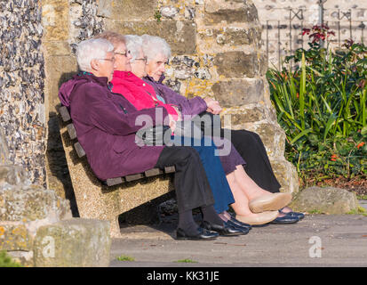 Gruppe von 4 älteren Frauen draußen sitzen auf einer Bank in warme Kleidung im Herbst in Großbritannien. Stockfoto