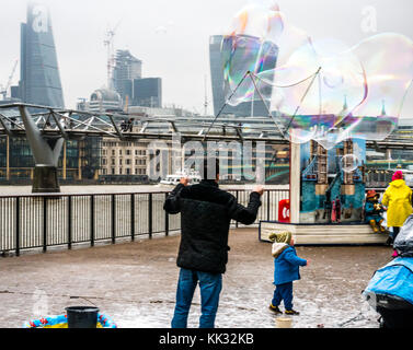 South Bank Themse weg Mann unterhalten Kinder und Leute, die große Blasen, London, England, Großbritannien mit Millennium Bridge, Wolkenkratzer Stockfoto