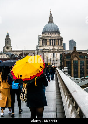 Menschen zu Fuß über die Millennium Bridge an regnerischen Tag mit hellen Sonnenschirmen für die St Paul's Cathedral und die City von London Schule, Themse, England, Großbritannien Stockfoto