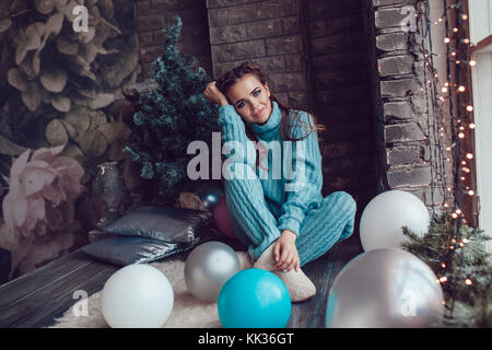 Schöne Frau sitzt zu Hause in der Nähe der Fenster mit Weihnachtsbeleuchtung. neues Jahr. Stockfoto