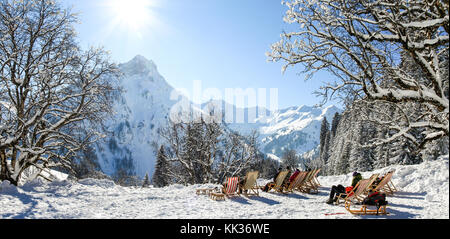 Gruppe von Menschen sitzen mit Liegestühlen im Winter Berge. Sonnenbaden im Schnee. Deutschland, Bayern, Allgäu, schwarzenberghuette. Stockfoto