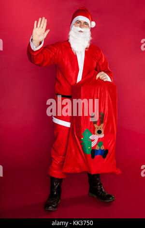 Der Weihnachtsmann winkte seine Hand und hielt einen Beutel voller Geschenke Stockfoto