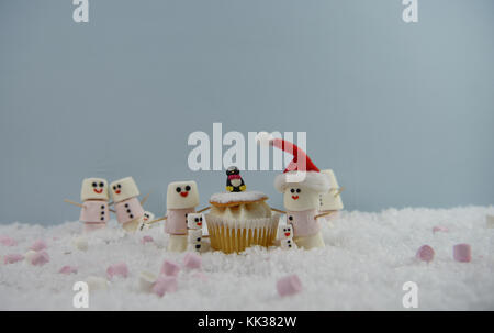 Weihnachten essen Fotografie Bild mit Sahne schwamm Fee Kuchen im Schnee mit Marshmallows, der so glücklich Schneemann und Santa Hut geformte platziert Stockfoto