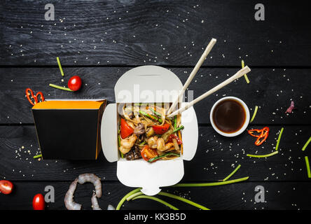 Wok. udon fry Nudeln mit Meeresfrüchten in einem Kasten auf schwarzem Hintergrund rühren. mit Stäbchen und Soße. Stockfoto