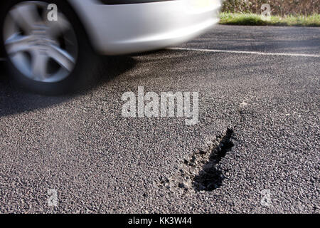 Auto vorbeifahren Schlagloch in der Straße, Sussex, England Stockfoto