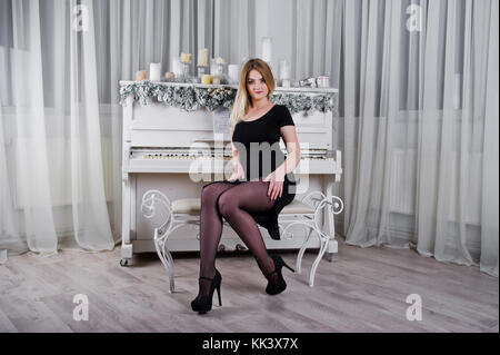 Blonde Mädchen in schwarzen Kleid, in der Nähe von Piano mit Weihnachten Kerzen Einrichtung in Weiß. Stockfoto