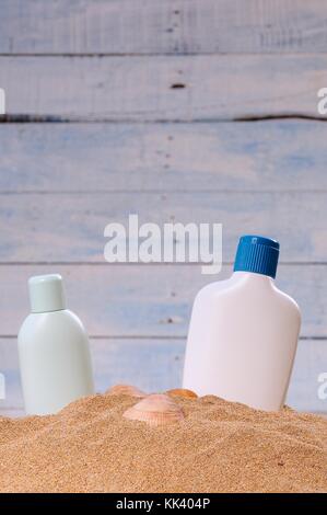 Zwei Flaschen Sun Lotion und Muscheln im Sand vor der blauen Wand Stockfoto